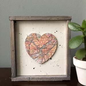 May include: A framed heart-shaped map of Philadelphia with black splatter paint on a white background. The frame is made of weathered wood.