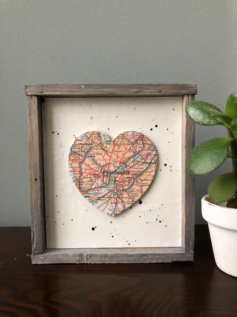 May include: A framed heart-shaped map of Philadelphia with black splatter paint on a white background. The frame is made of weathered wood.