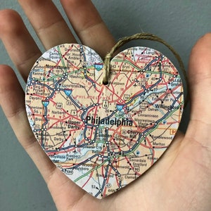 May include: A heart-shaped wooden ornament with a map of Philadelphia, Pennsylvania printed on it. The ornament has a string attached for hanging.