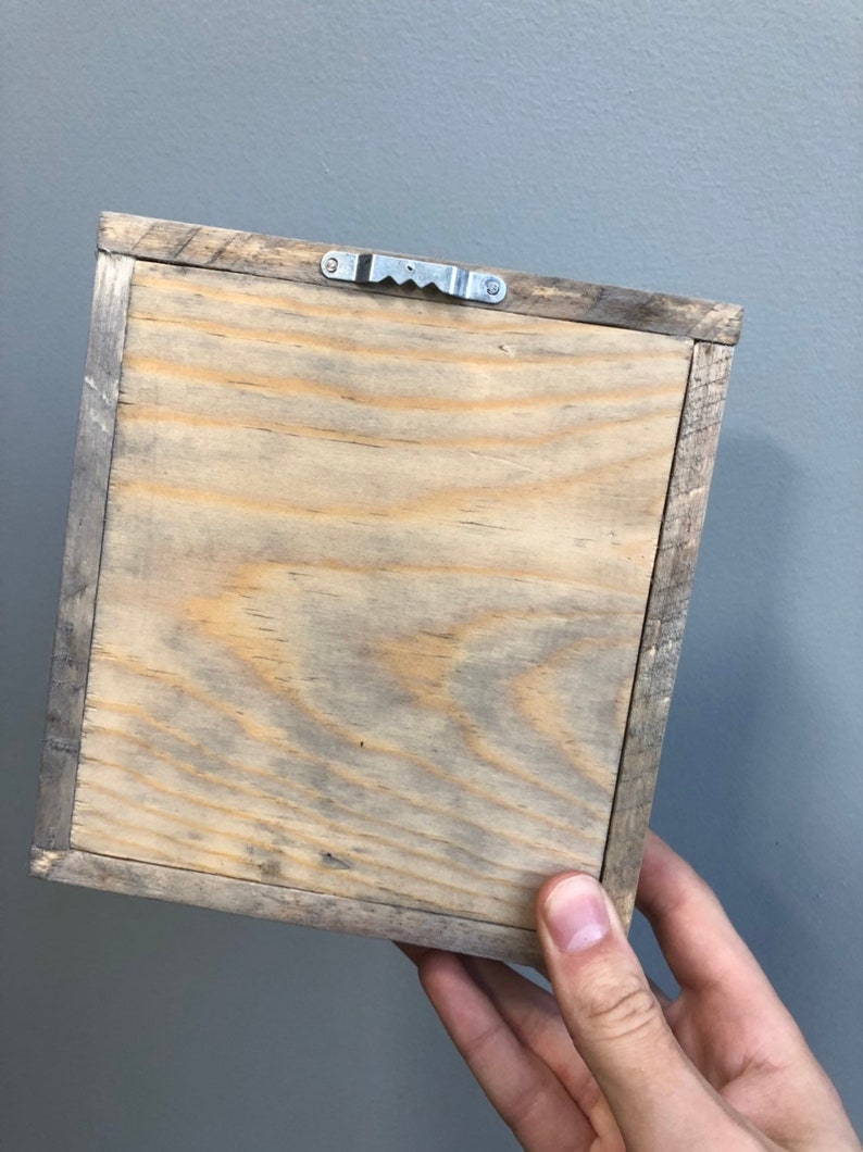 May include: The back of a wooden picture frame with a metal hanging hook. The frame is made of natural wood with a light brown finish.