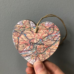 May include: A wooden heart-shaped ornament with a map of Philadelphia, Pennsylvania printed on it. The ornament has a twine string for hanging.