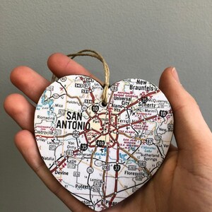 May include: Heart-shaped wooden ornament featuring a map of San Antonio, Texas. The ornament includes the city name and surrounding areas, with a twine loop for hanging. A unique souvenir or gift.