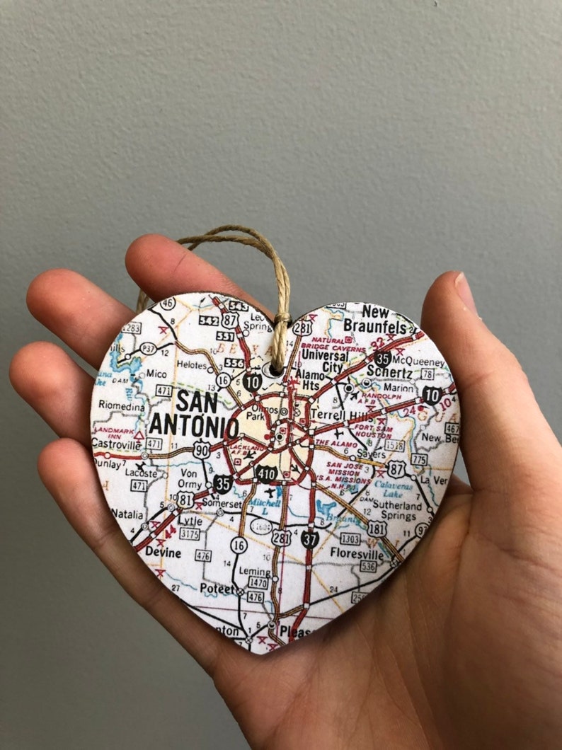 May include: Heart-shaped wooden ornament featuring a map of San Antonio, Texas. The ornament includes the city name and surrounding areas, with a twine loop for hanging. A unique souvenir or gift.