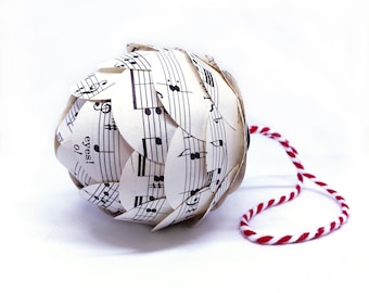 May include: A white Christmas ornament shaped like a pine cone, made from pages of sheet music. The ornament has a red and white twine hanger.