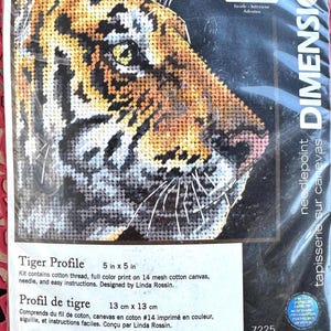 May include: A Dimensions needlepoint kit titled Tiger Profile featuring a cross-stitch design of a tiger's face in orange, black, and white. The packaging includes a thread organizer, cotton thread, a needle, and 5 in x 5 in cotton canvas.