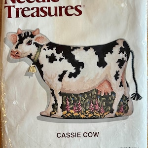 May include: A Needle Treasures needlepoint kit for a Cassie Cow stuffed figure. The packaging features a black and white cow with a bell, measuring 14 inches by 10 inches. The kit includes canvas, wool tapestry yarn, cotton floss, and a needle.