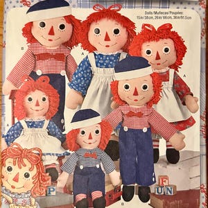 May include: Simplicity 8043 sewing pattern for Raggedy Ann and Andy dolls. The package features illustrations of dolls in various outfits, including blue and red gingham, floral prints, and hats. Sizes include 15, 26, and 36 inches for the dolls.