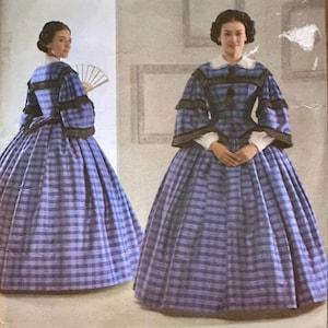 May include: Simplicity sewing pattern featuring a Civil War era dress. The pattern shows a woman in a blue and white plaid dress with long sleeves and a full skirt. The pattern includes size information and the Simplicity logo.
