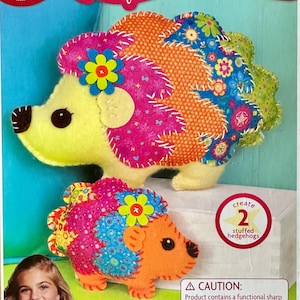 May include: American Girl Crafts Sew & Stuff Kit featuring two plush hedgehogs made from colorful patterned fabric with felt accents. The kit includes 23 pieces to create one large and one mini stuffed hedgehog, each decorated with a felt flower.