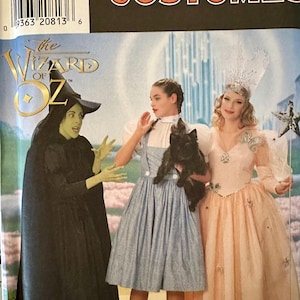 Puede incluir: Patrón de disfraces Simplicity con personajes de El Mago de Oz. La imagen muestra a tres personas vestidas como la Bruja Malvada, Dorothy y Glinda. El patrón incluye tallas 12, 14 y 16.