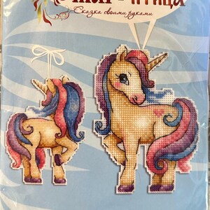 May include: Cross-stitch kit featuring two unicorn designs with tan bodies, pink cheeks, and flowing manes and tails in pink and blue. The kit includes the text "Жар-птица" and "Сказка своими руками". Finished sizes are 4¾" x 3½".