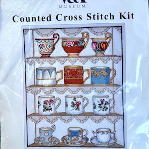 May include: A V&A Museum counted cross stitch kit featuring a teacup sampler design. The packaging displays a grid of twelve illustrated teacups on shelves with lace trim. The text reads V&A Museum, Counted Cross Stitch Kit, and Teacup Sampler.