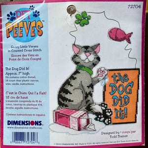 May include: A cross-stitch kit with a design of a grey cat wearing a green collar, holding a sign saying "the DOG DID it!". The kit includes cotton thread, a 14-count clear plastic canvas, wire, needle, and instructions. The finished piece is approximately 18 cm high.