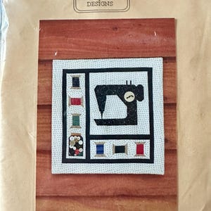 May include: A sewing machine paper foundation pattern with a black sewing machine design and thread spools. The pattern size is 28.58 cm x 29.85 cm. The MH Designs logo is at the top.