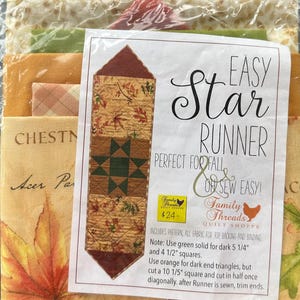 以下が含まれることがあります： Easy Star Runnerのキルトプロジェクト用の生地キット。キットには生地とパターンが含まれています。ランナーのデザインは、星のパターンと秋の葉のモチーフが特徴です。パッケージのテキストには「Perfect for Fall」と「Easy Star Runner」と書かれています。