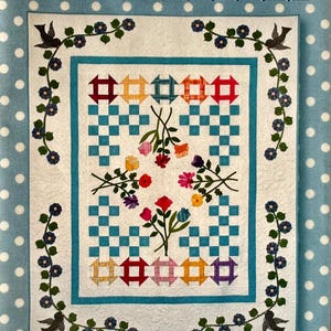 May include: A quilt with a central design featuring a checkerboard pattern in white and teal, surrounded by colorful blocks and floral embroidery. The quilt is framed by a teal border and a border of birds and flowers. The text "Just Picked" and "Painted Pony 'n Quilts" are visible.
