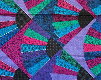 May include: A fabric featuring a repeating fan pattern in vibrant shades of magenta, teal, purple, and black. Each fan segment displays intricate floral and geometric motifs. A white selvage edge at the bottom includes the text A V.I.P Print By JOAN MESSMORE © Cranston Print Works Co. and a 12-inch ruler.