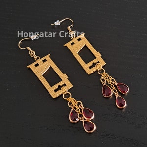 May include: Gold guillotine earrings with dangling red teardrop crystals. The guillotine is a symbol of the French Revolution.