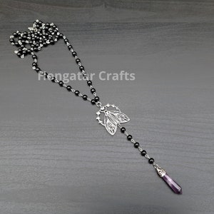 May include: A necklace featuring a chain of small black beads, a silver-toned moth pendant, and a pointed purple crystal drop. The text Fiongatar Crafts is visible in the center. The design includes a long chain segment extending below the moth.