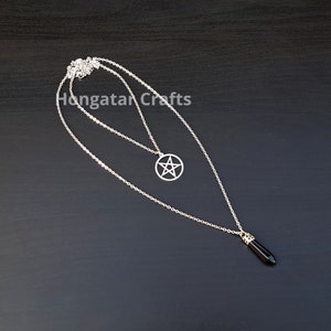 Puede incluir: Un collar de cadena de plata con dos colgantes. Un colgante es un pentagrama de plata y el otro es una piedra preciosa negra.