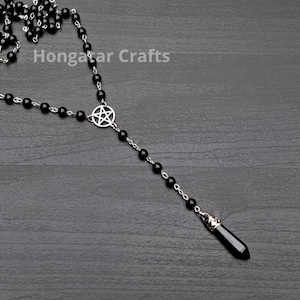 Puede incluir: Un collar de cuentas negras con un dije de pentagrama plateado y un dije de punta de cristal negro. El collar está sobre una superficie de madera gris. Hongatar Crafts