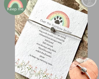 May include: A memorial card with a rainbow and paw print design, and the text "Over the Rainbow Bridge." A silver bracelet with a paw print charm is also shown. The card includes a poem about remembering loved ones.
