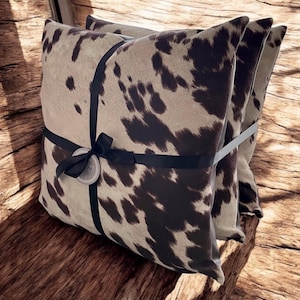 May include: Two brown and white cowhide patterned throw pillows with black ribbon tied around them.