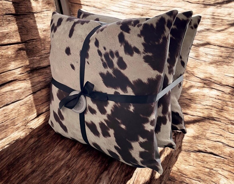 May include: Two brown and white cowhide patterned throw pillows with black ribbon tied around them.