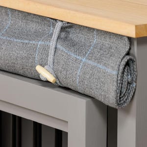 May include: A gray and white patterned blanket is rolled up and tied with a wooden toggle. The blanket is on top of a gray wooden crate with a wooden top.