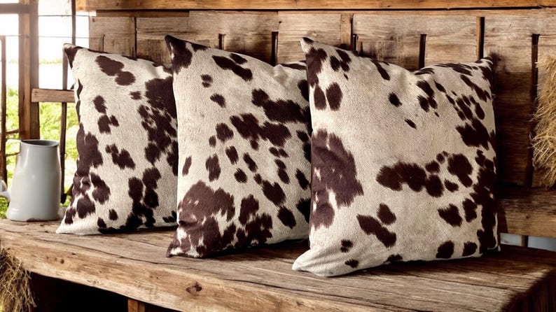 May include: Three brown and white cowhide patterned throw pillows on a wooden bench.