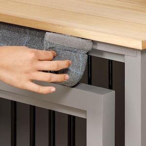 May include: A gray wooden dog crate with a gray fabric cushion on top. The cushion is secured with a gray velcro strap. The crate has a wooden top that can be lifted to access the inside.