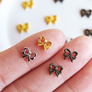 May include: Assortment of gold and black metal bow charms. The charms are small and delicate, perfect for adding a touch of elegance to crafts and jewelry.