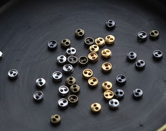 Può includere: Un piatto nero pieno di bottoni a due fori in oro, argento e nero.
