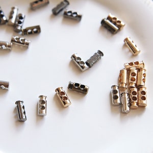 May include: Assortment of metal toggle clasps in silver, gold, and bronze finishes. The clasps have two holes and are designed for use with cords or straps.