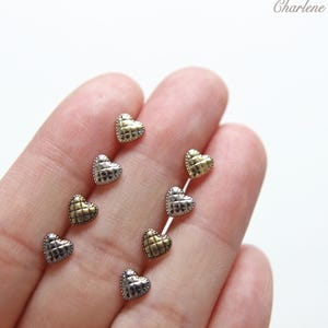 May include: Close-up of several heart-shaped stud earrings in gold and silver tones. The earrings have a quilted texture and are arranged in a hand. The word "Charlene" is written in cursive in the upper right corner.