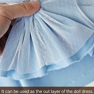 Puede incluir: Primer plano de una tela azul claro con una superposición de malla blanca. La malla está recogida y fruncida, creando un aspecto delicado y aireado. Se puede utilizar como capa exterior de un vestido de muñeca.