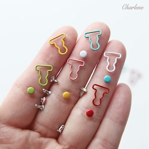 May include: Assortment of colorful metal T-shaped clasps and silver metal snaps. The clasps are in various colors including red, yellow, blue, green, and pink. The snaps are silver with a small colored dot on the top.