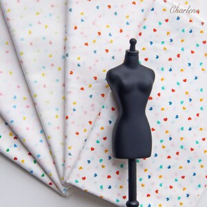 May include: A stack of white fabric with a small, colourful heart pattern. The fabric is folded in a fan shape and a black mannequin is standing in front of it.
