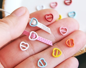 May include: Assortment of colorful heart-shaped metal buckles with a white, pink, and blue leather strap. The buckles are perfect for adding a touch of whimsy to crafts and DIY projects.