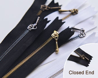 May include: A close-up of three zippers, two black and one white, with metal pulls. The zippers are closed at the bottom and have a "Closed End" label.