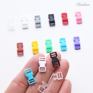 Könnte beinhalten: Sortiment an Kunststoff-Seitenschnallen in verschiedenen Farben, darunter Schwarz, Weiß, Rot, Gelb, Grün, Blau, Hellblau, Lila und Klar. Die Schnallen sind etwa 2,5 cm lang.