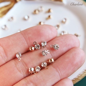 Könnte beinhalten: Nahaufnahme einer Hand, die eine Vielzahl von klaren Kristall-Strassteinen mit goldenen und silbernen Fassungen hält. Die Strasssteine sind klein und rund und haben eine glänzende Oberfläche.