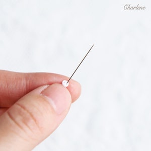 May include: A white bead is threaded onto a thin, silver needle.