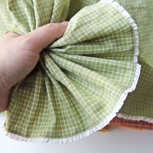 May include: A green and white checkered fabric with a white lace trim. The fabric is folded and held in a hand.