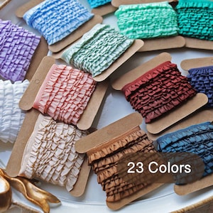 May include: Assortment of 23 colours of ruffled trim ribbon spooled on brown cardboard cards. The trim is made of a soft, textured fabric.