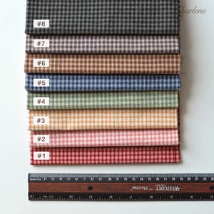 Pode incluir: Uma seleção de oito amostras de tecido em várias cores, cada uma com um pequeno padrão xadrez. As amostras são rotuladas com números de #1 a #8. Uma régua com medidas em centímetros é colocada na parte inferior, mostrando as dimensões do tecido.