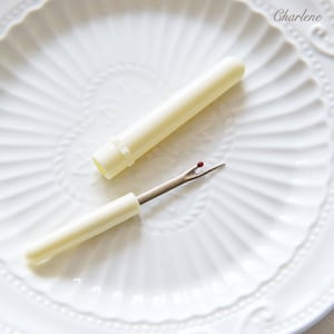 Puede incluir: Un cortador de hilo de plástico blanco con una punta roja, abierto y cerrado, en un plato blanco con un borde decorativo.