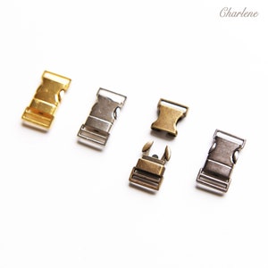May include: Four metal clasps in different finishes: gold, silver, antique brass, and gunmetal. The clasps are all the same size and shape, with a rectangular body and a small, rectangular buckle.