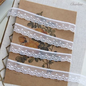 May include: White lace trim with a scalloped edge and small dots. The lace is shown in three rows on a brown background.