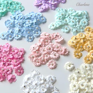 May include: A collection of colorful paper flowers in shades of pink, blue, yellow, green, and white, each adorned with a pearl center. The flowers are arranged in clusters, with the name "Charlene" in the upper right corner.